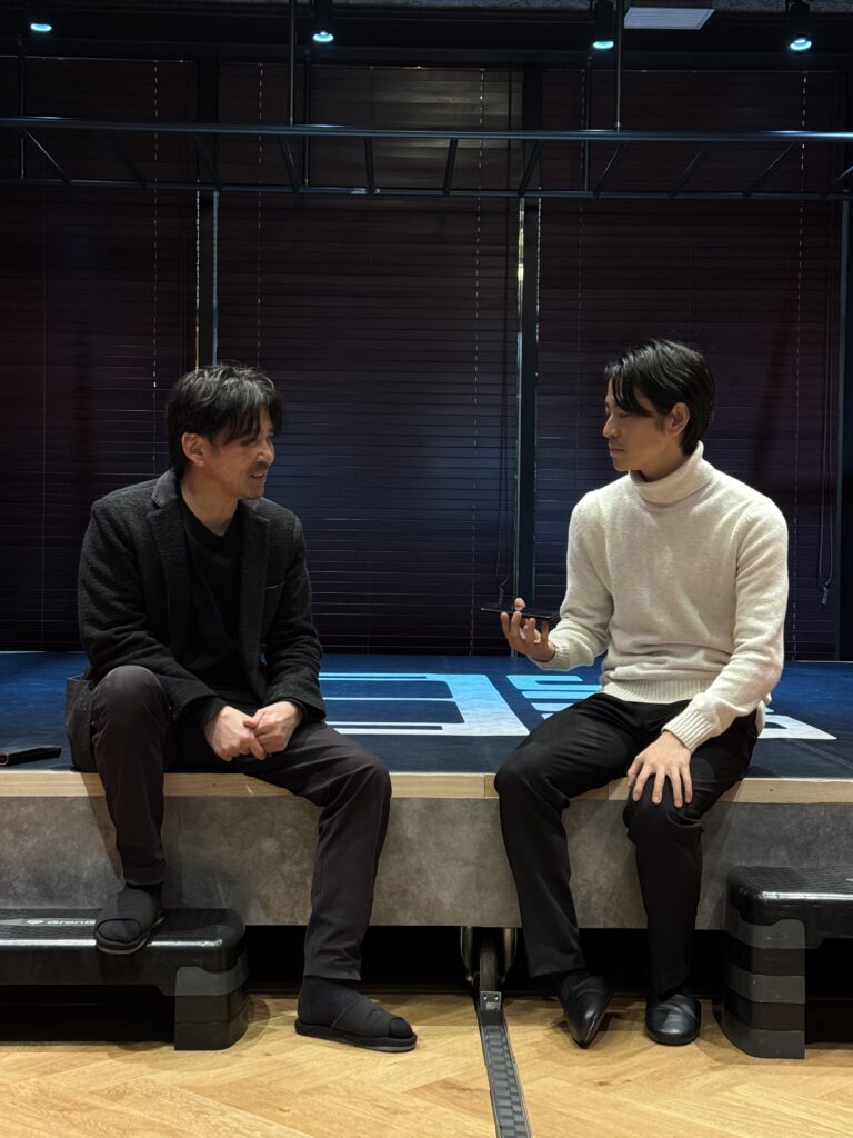 ジムのリング前のスペースに座り、向かい合って会話を交わすNOBUと池田代表。落ち着いた照明の中で対談している様子。