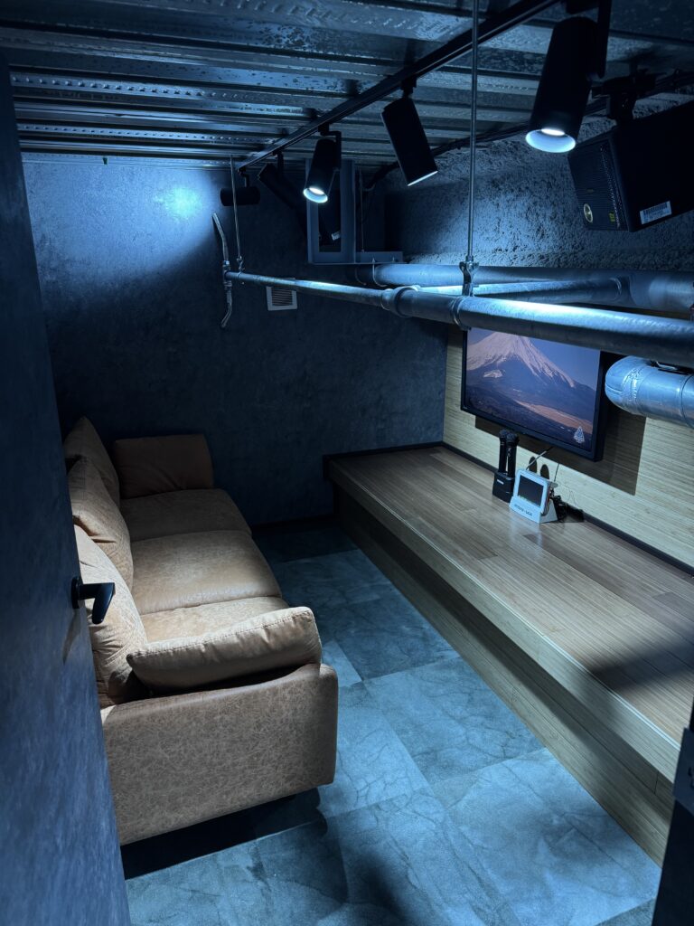 OYG銀座ジムに設けられた隠れ家風のカラオケルーム。青いライトに照らされた壁面、むき出しの配管、無骨な天井…そうしたラフな素材感の中に、音響のクオリティを追求した設備が丁寧に組み込まれている。高出力のスピーカー配置や吸音バランスまで計算され、歌うときの“音の気持ちよさ”が際立つように設計された空間。トレーニングとはまったく異なる、OYG独自の“音を楽しむための部屋づくり”を象徴している。