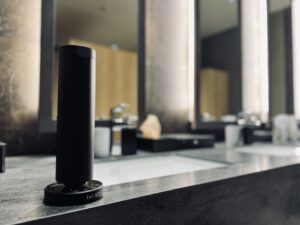 ホテルのような洗練された洗面空間のカウンターに置かれた黒いLei業務用ディフューザー。柔らかな照明と陰影の中で静かに香りを広げている。