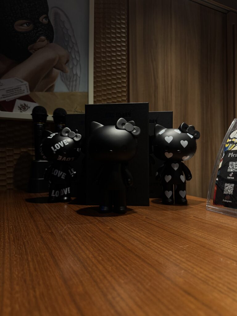 黒を基調としたキャラクター・フィギュアが木製カウンターに並び、背後には人物を描いたアートワークが飾られている。