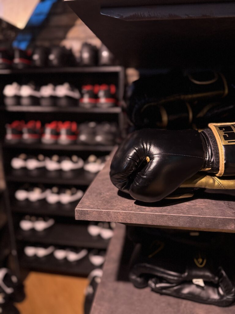 棚に置かれた黒とゴールドのボクシンググローブ。背景には整然と並んだトレーニングシューズが見える。