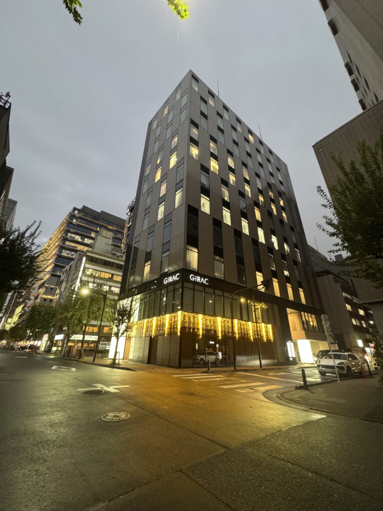 夕方の銀座でライトアップされたビル「GIRAC」。外観の柔らかなイルミネーションが街角を照らしている。