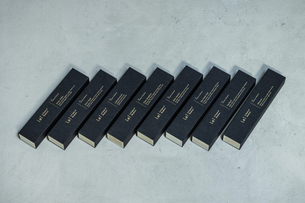 Eight matte-black Lei “In Praise of Shadows” incense boxes lined up on a light-gray surface, each labeled with a different scent name in gold foil.