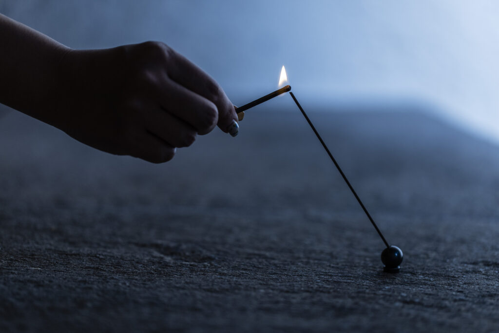 手に持ったマッチでお香に火を灯している瞬間。一本のお香が斜めに立ち、先端が燃えている様子