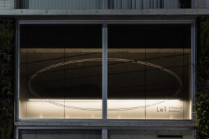 The exterior of Lei In Praise of Shadows Flagship Store at night, with an oval outline and the store’s logo softly illuminated on the large glass window.