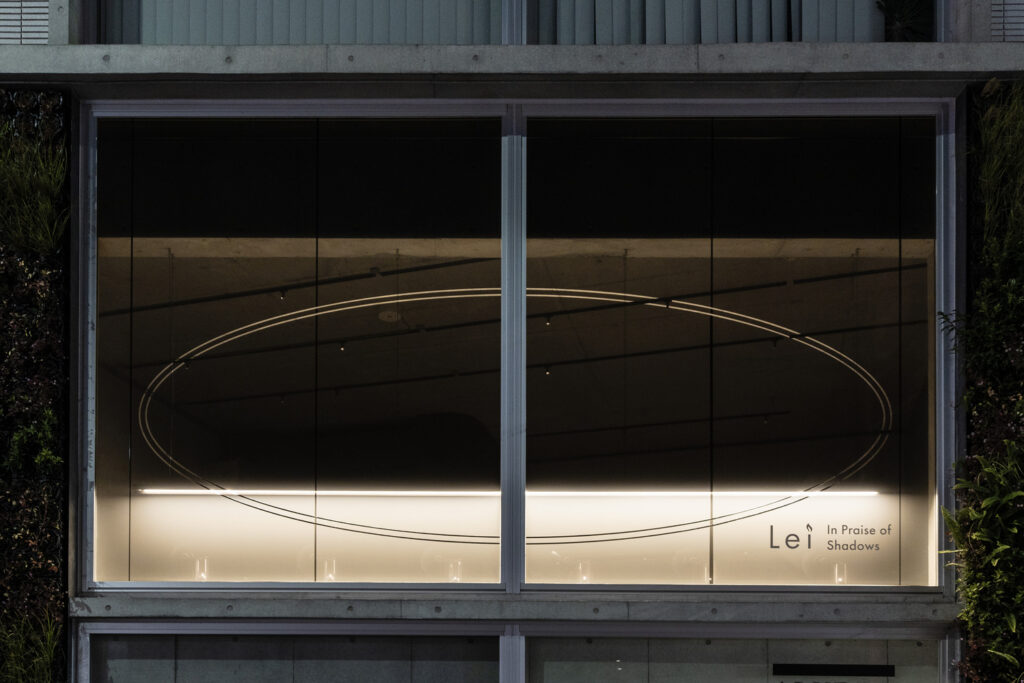 Lei In Praise of Shadows Flagship Storeの外観。大きなガラス窓に楕円のラインと店名ロゴが灯る夜景