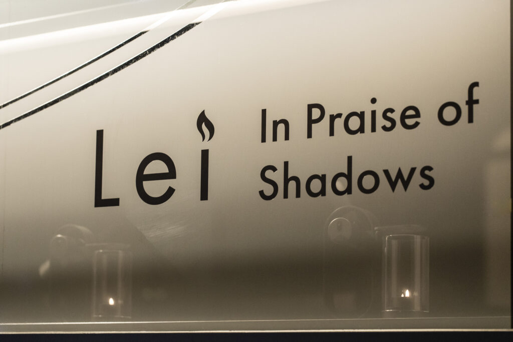 “Lei In Praise of Shadows” logo printed on a storefront window, with candlelight reflections in the glass.
