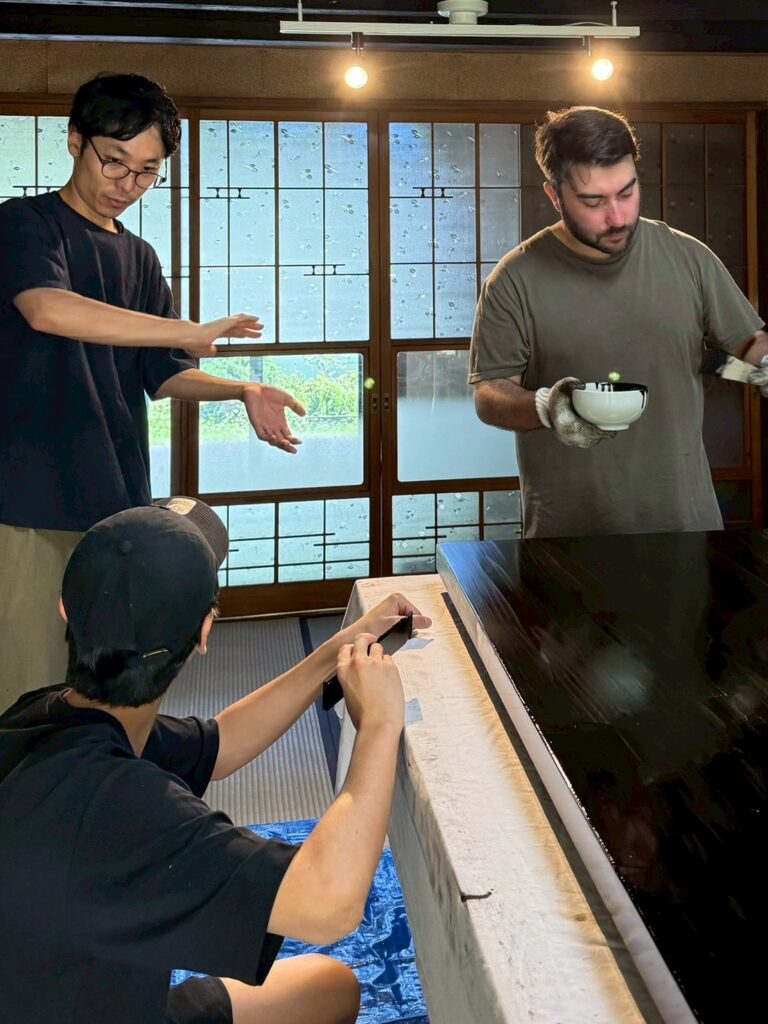 Team reviewing and applying urushi lacquer to a display stand surface during the making of Lei In Praise of Shadows Flagship Store.