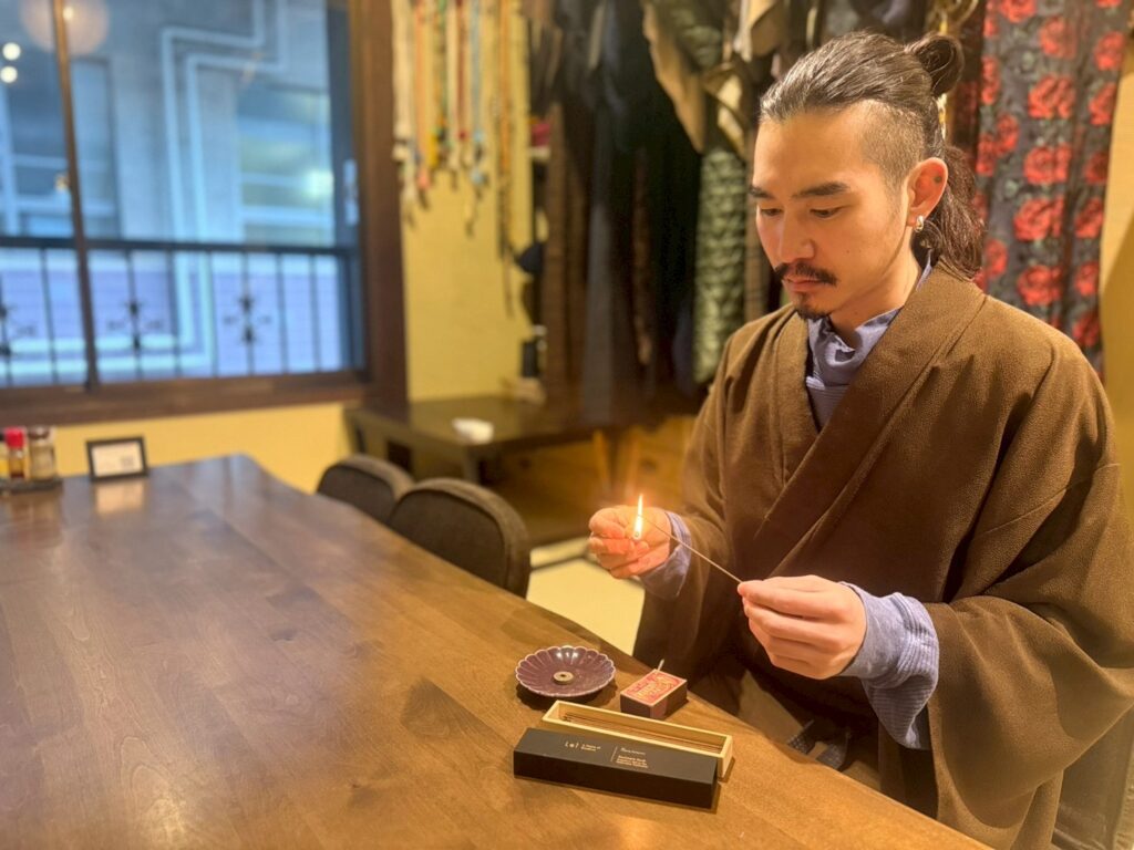 巧流-call-の店内で、着物姿の元山巧大さんがLeiのお香に火を灯している(テーブル上に香皿とお香)