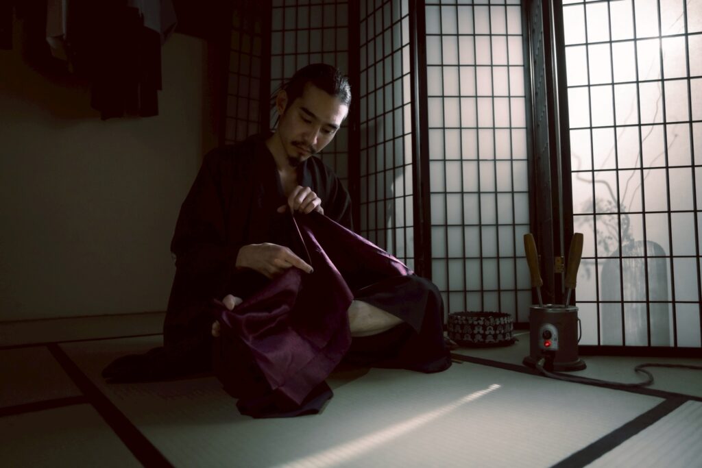 畳の部屋で、着物姿の巧流-call-代表 元山巧大さんが布を手にしながら作業する様子(障子越しの光)