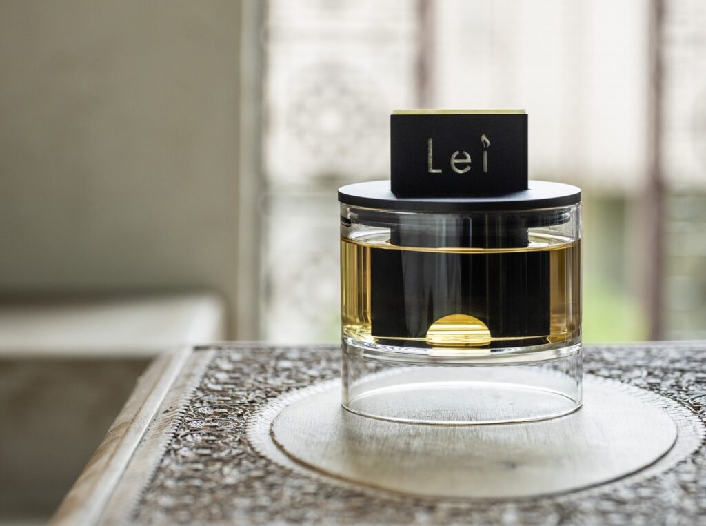 窓辺のテーブルに置かれたLei Card Diffuser。透明ガラス容器に琥珀色のオイルと黒いトップパーツ、Leiロゴプレート。