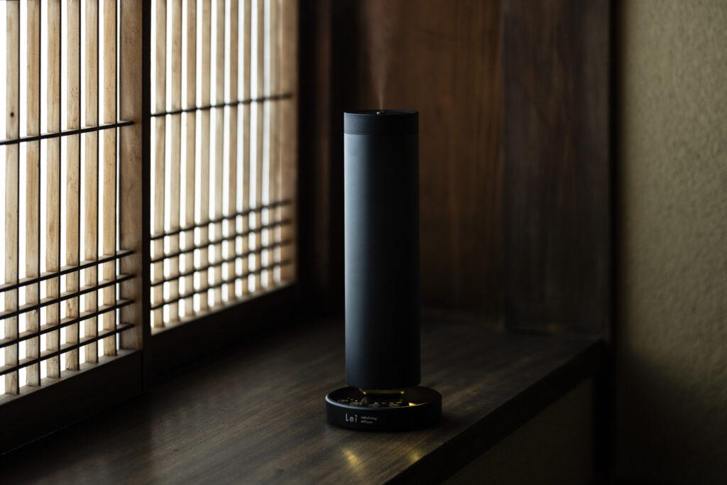 Lei professional diffuser placed on a wooden ledge beside a shoji-style window, releasing a subtle mist.