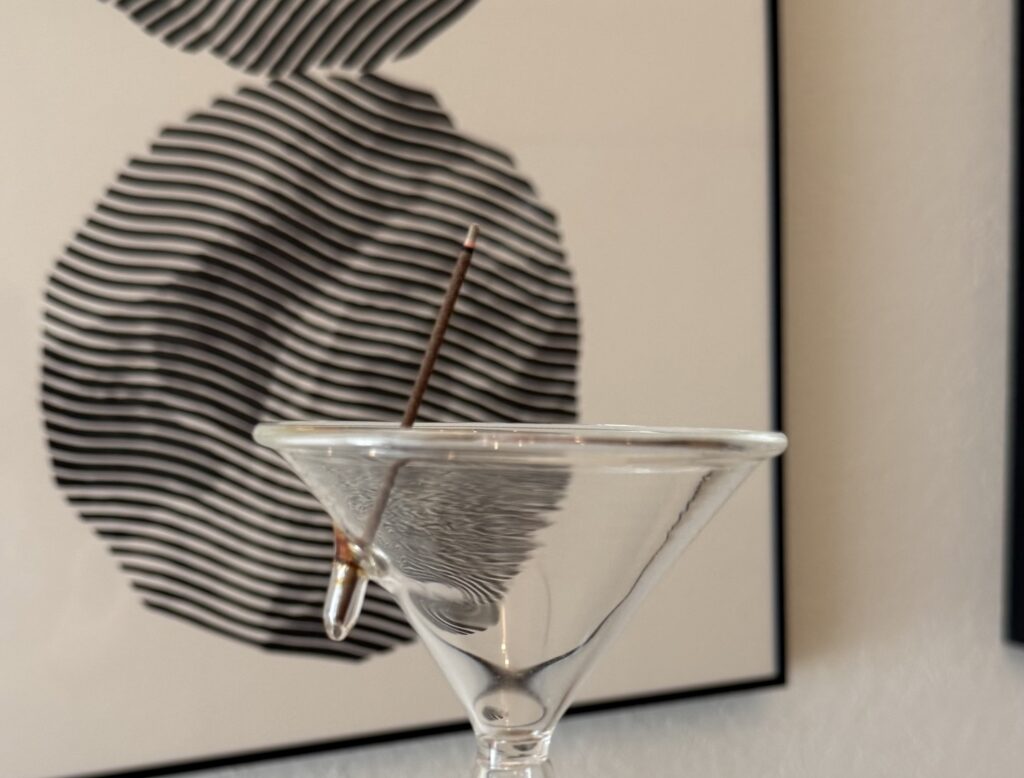 ガラスの香立てに立てたお香。背景にモノクロのアートが見える。