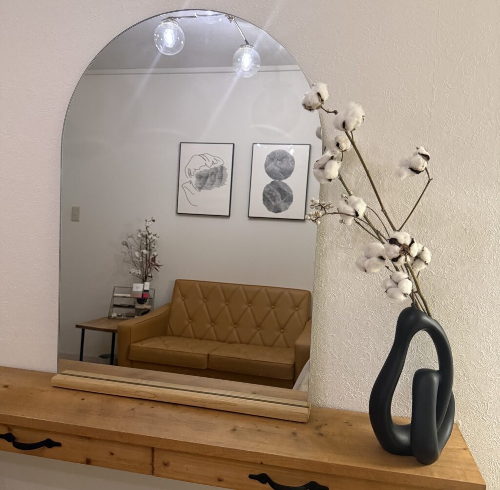 サロンの待合スペース。丸い鏡にソファとアートが映り、花器にコットンフラワーが飾られている。