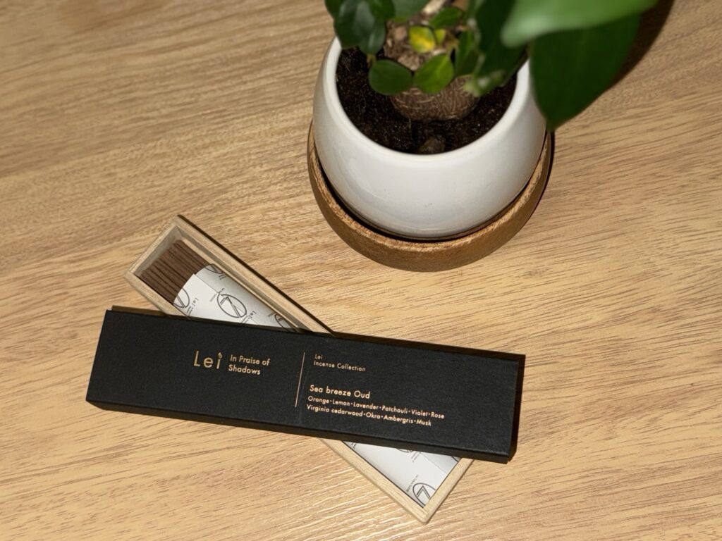 木のテーブルに置かれたLei Incense Collection「Sea breeze Oud」の箱と桐箱。横に白い鉢植え。