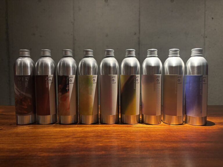 拭き漆加工を施したカウンターに並ぶLeiのアルミボトル9本（KUON、Fig Royale、Honey Amber、Green Symphony、White Tea、Citrus Wood、Spicy Jasmine、Cashmere Musk、Sea breeze Oud）
