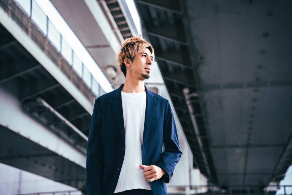 高架下でジャケット姿の藤光謙司さんが立ち、遠くを見つめているポートレート。