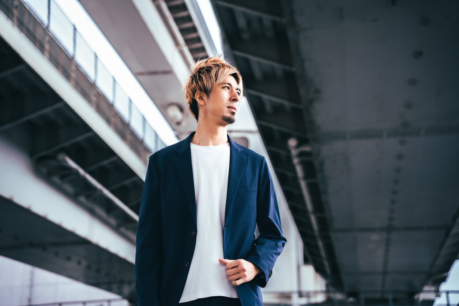 高架下でジャケット姿の藤光謙司さんが立ち、遠くを見つめているポートレート。