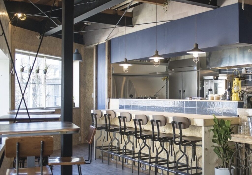 仙川のイタリアンレストラン「trattoria filo」の店内。オープンキッチンのカウンター席とハイチェア、ペンダントライトが並ぶ様子。