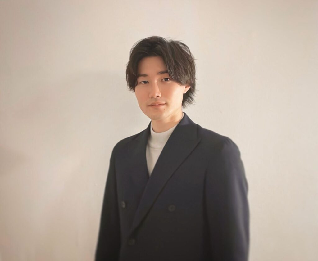 ネイビーのダブルジャケットを着た山田 長太さんのポートレート。白い背景の前で正面を向いて立っている。