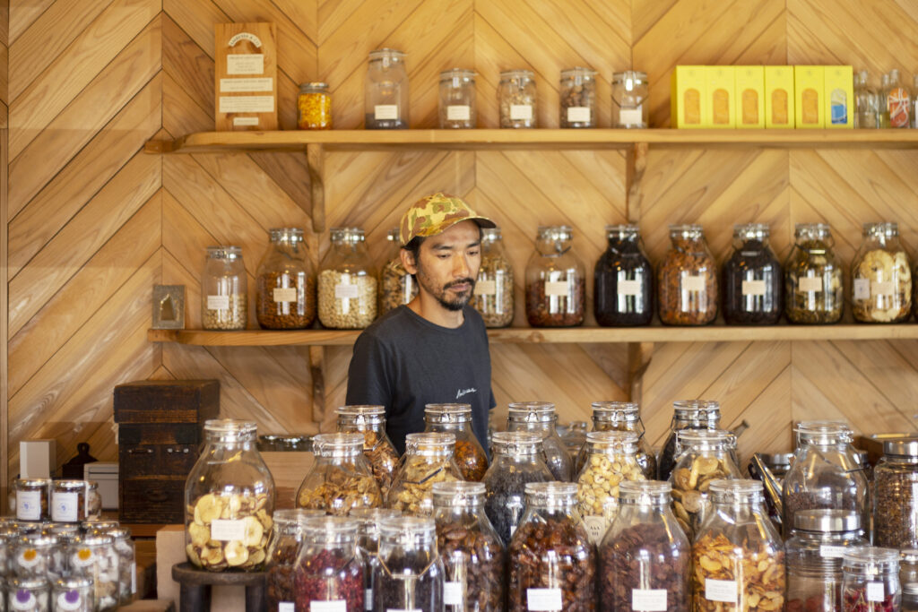 オーガニックドライフルーツやローナッツの瓶が並ぶ店内で立つ、AMBESSA & CO代表・君島悠矢さん