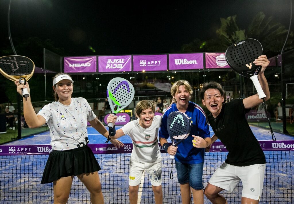 パデルコートで参加者と並び、ラケットを掲げて笑顔を見せる五味亮将さん