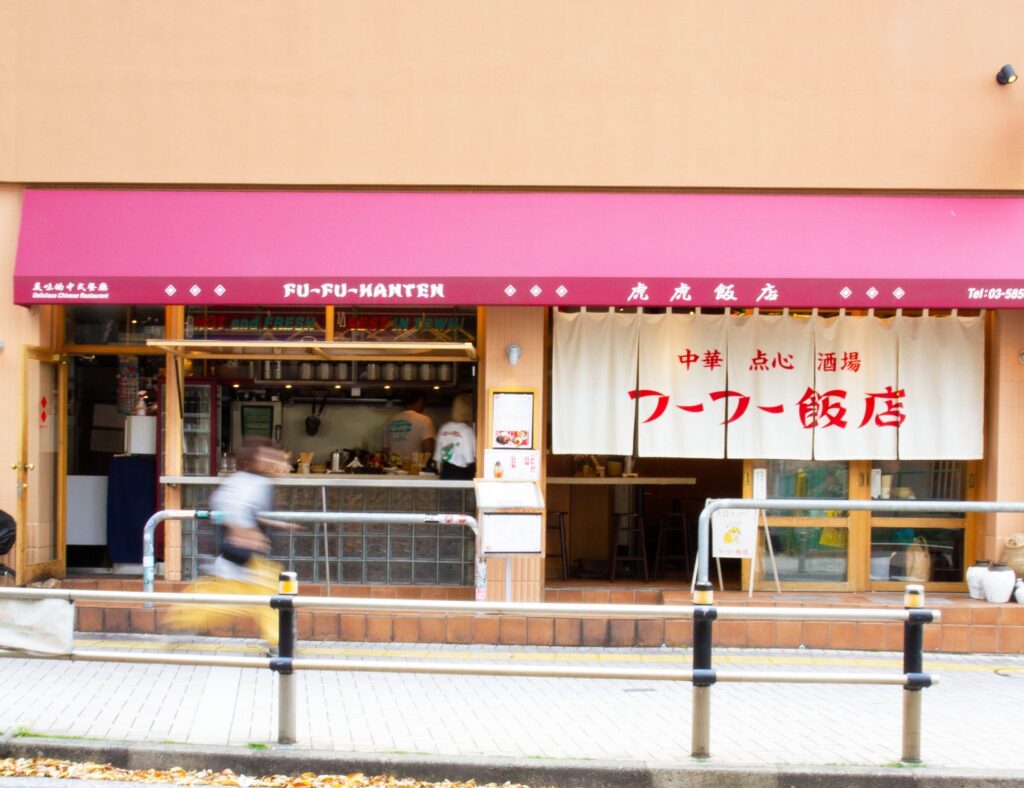 錦糸町のフーフー飯店の外観。赤い看板と暖簾、通りを横切る人の動きが重なる様子