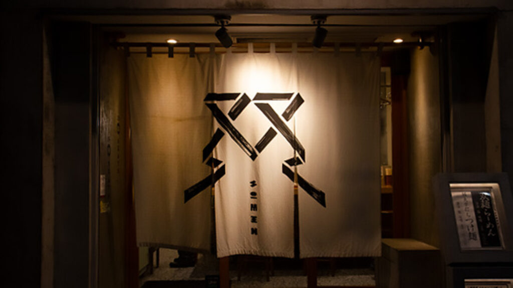 暖簾に「双麺」とロゴが描かれた夜の店舗入口。柔らかな光が奥から漏れる様子