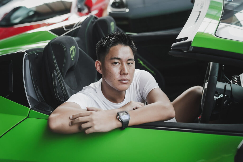 スポーツカーに腰をかけ、まっすぐカメラを見つめる富田一輝選手