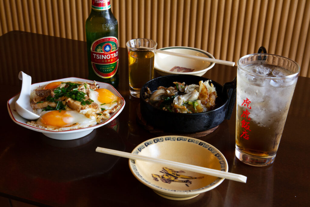 フーフー飯店の食卓。青島ビール、ハイボール、餃子と牡蠣料理、目玉焼きが並ぶ町中華の食事風景