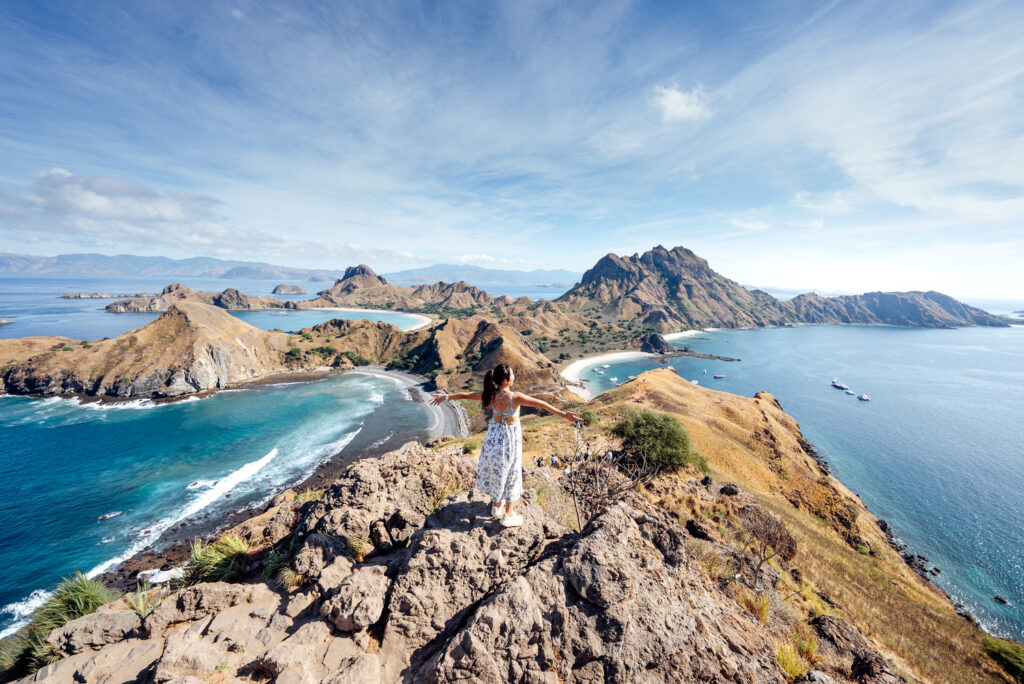 海と島々を望む高台に立ち、両腕を広げるSUMMYさんの後ろ姿