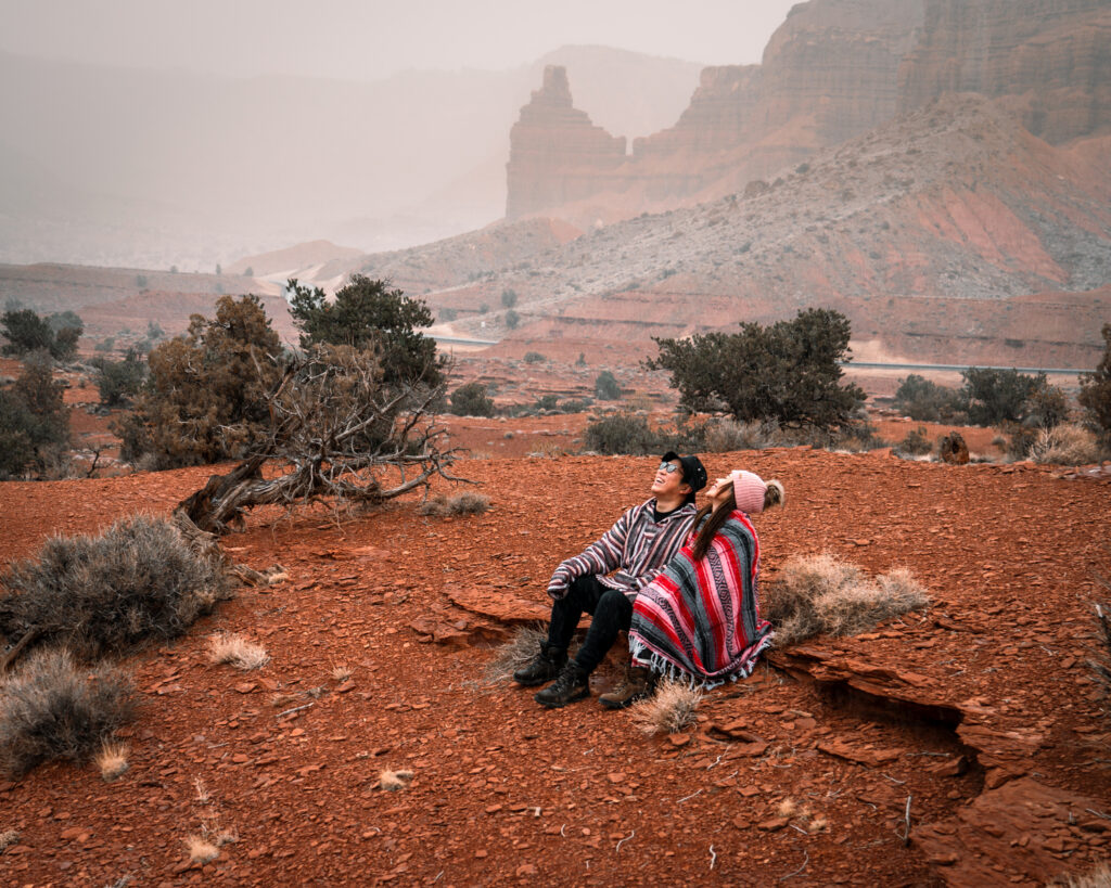 赤い大地と岩山が広がる風景のなか、並んで座り空を見上げるZEOさんとSUMMYさん