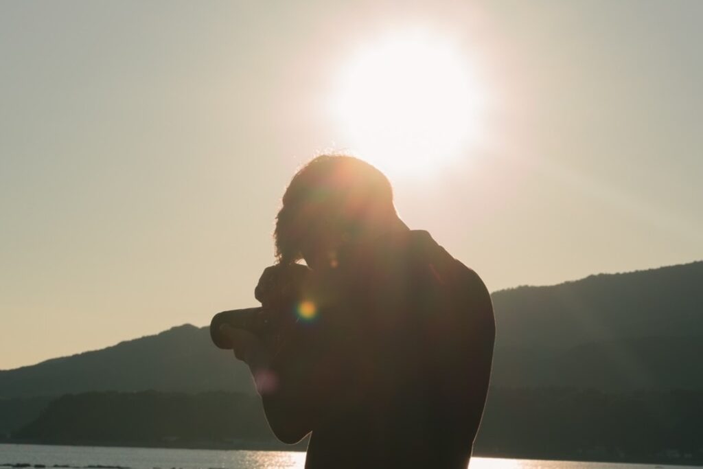 逆光の中、湖畔でカメラを構える塚本直純さんのシルエット