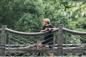 緑に囲まれた橋の上でカメラを手に立つ塚本直純さん