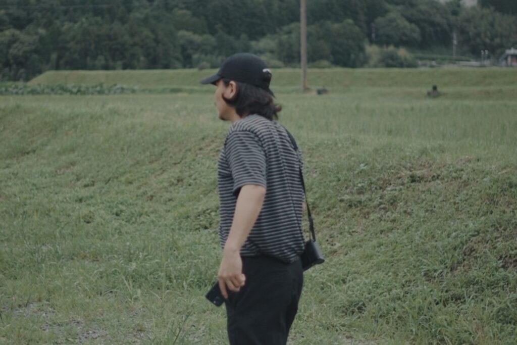 草原の中を歩く塚本直純さんの後ろ姿