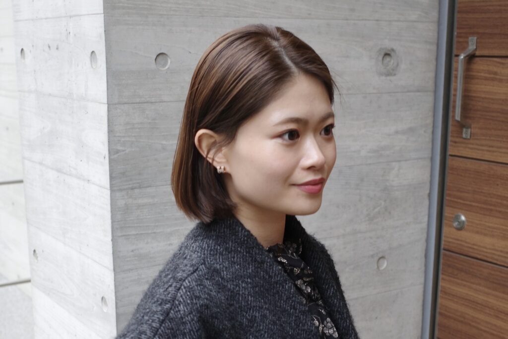 コンクリート壁の前に立ち、やわらかな表情を見せる藤井由香里さんのポートレート