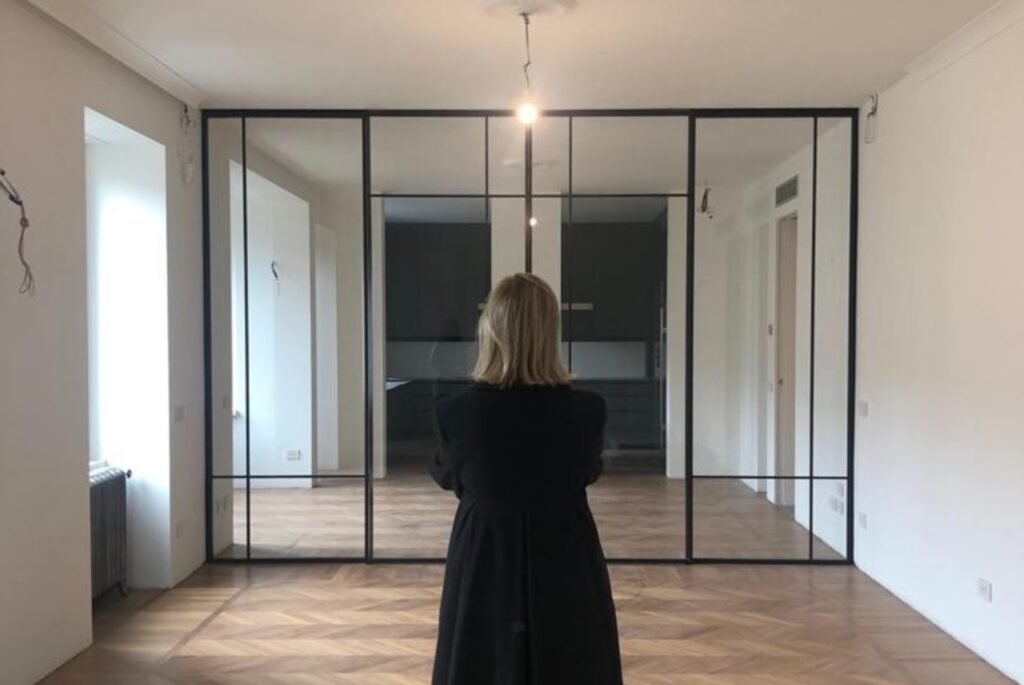 黒いフレームのガラス間仕切りがある室内で、Isabella Goldmannさんが立ち止まり空間を見つめている後ろ姿