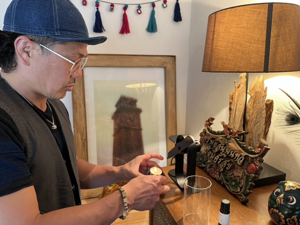 橋本淳平さんがnon electric aroma diffuserのキャンドルに火を灯す様子。室内の棚の上で香りの準備をしている風景