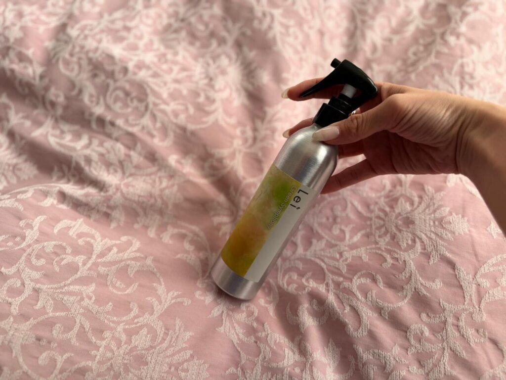 Lei Room Sprayをベッドの上で手に取る様子
