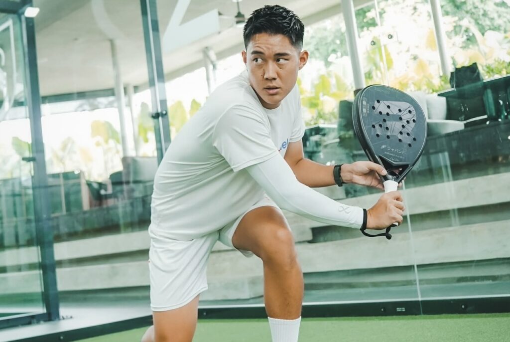ガラス張りのパデルコートで低く構え、左方向を見据える富田一輝選手