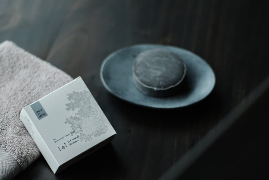 Botanical Craft Soapのパッケージと黒い石けんを、陰影のある空間で撮影したイメージ