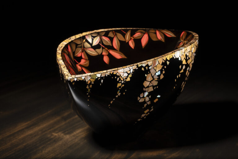 Maki-e Sacred Water Vessel “Glow,” a black urushi vessel with gold and red decorative details, photographed in shadow and warm light.