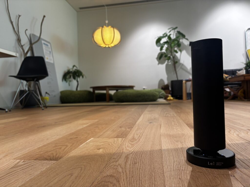 株式会社EmpaCのオフィスに設置されたLei業務用ディフューザー。木の床と照明、植物のある空間に黒いディフューザーが置かれている。