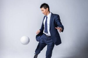 スーツ姿で白いサッカーボールを扱う安英学さんのポートレート