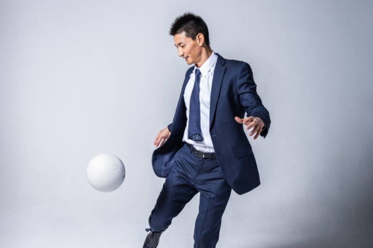 スーツ姿で白いサッカーボールを扱う安英学さんのポートレート