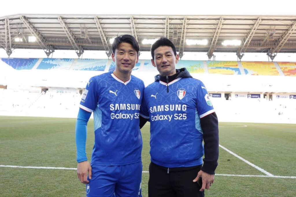 スタジアムで青いユニフォームを着た選手と並ぶ安英学さん