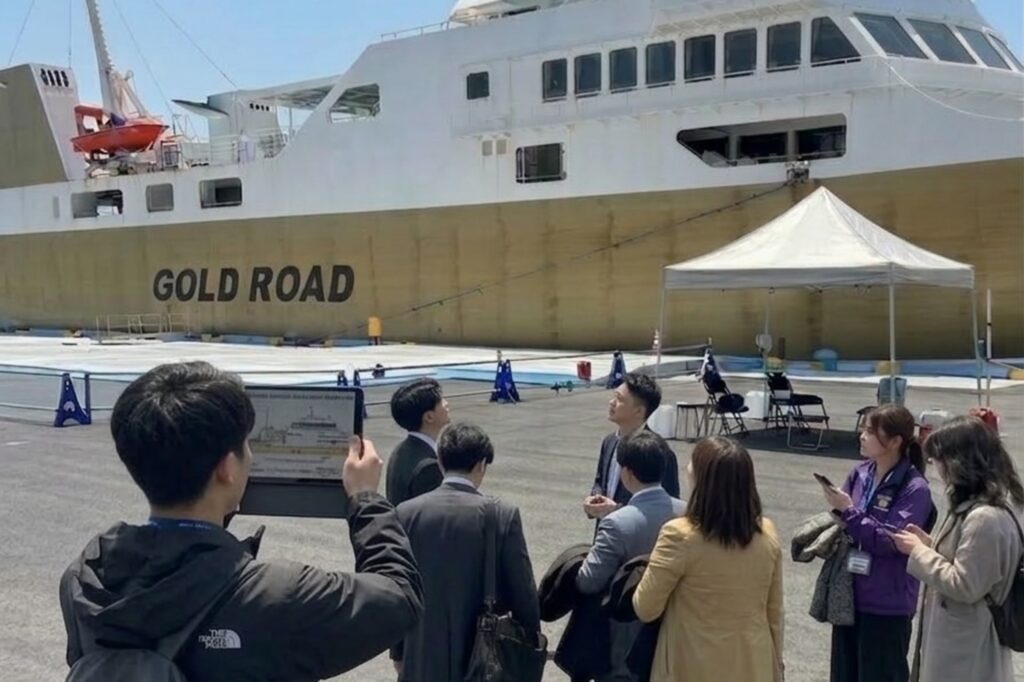 大型貨物船の前で、参加者が港湾施設の説明を受けている様子。