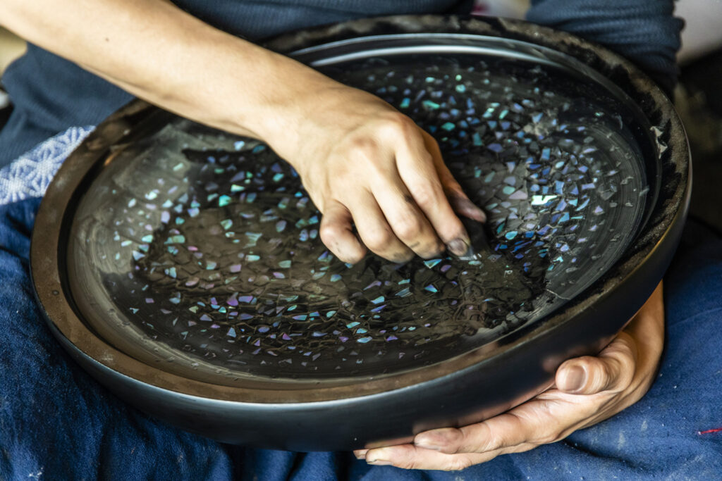 Urushi artist Tasuku Murose working on a lacquer surface with iridescent raden shell inlay.