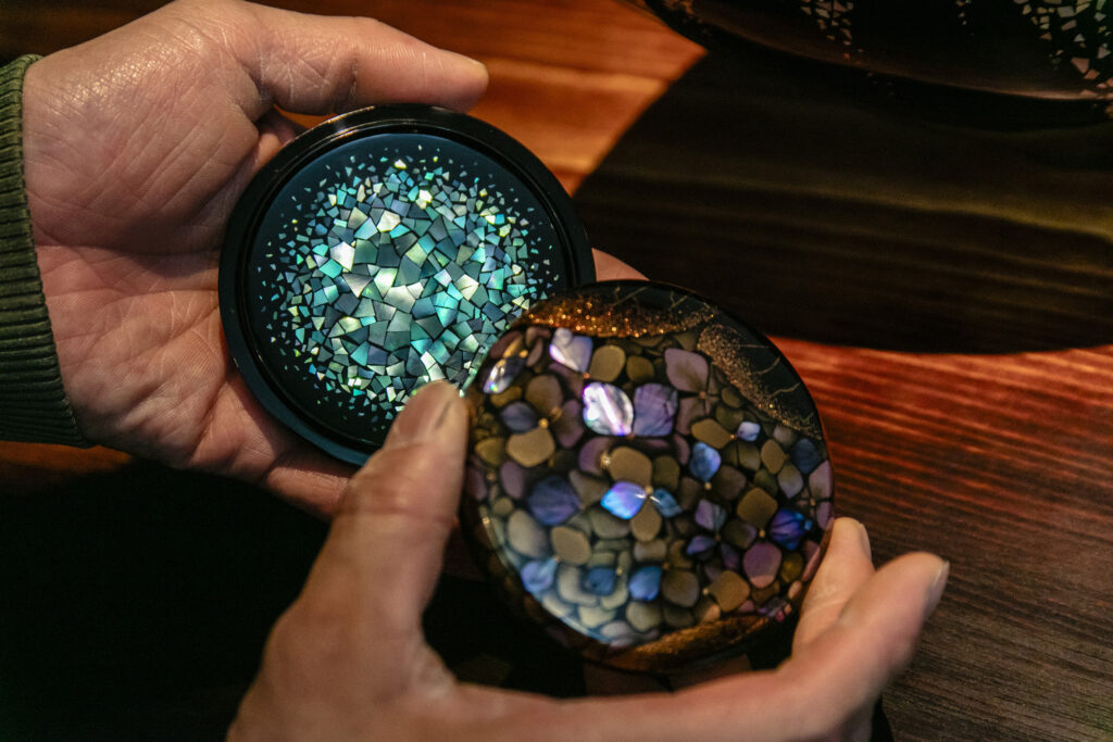 手のひらの上で、漆芸家 室瀬祐さんの螺鈿と蒔絵の小作品が光を受けて青や紫に輝いている様子。