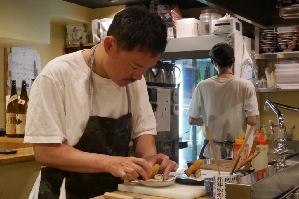 飲食店「吉」の厨房で料理を盛り付けるオーナーの小峰丈晴さん